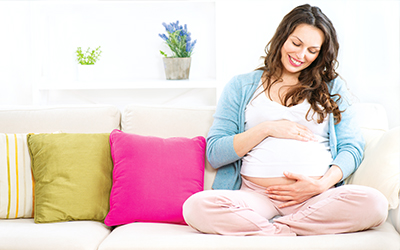 A woman sitting on a couch holding her pregnant belly