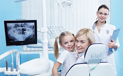 Healthy dental patients smiling with a picture of an x-ray hanging in the background