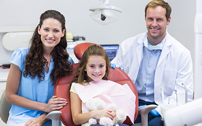 A dentist with a young girl and mother in dental chair